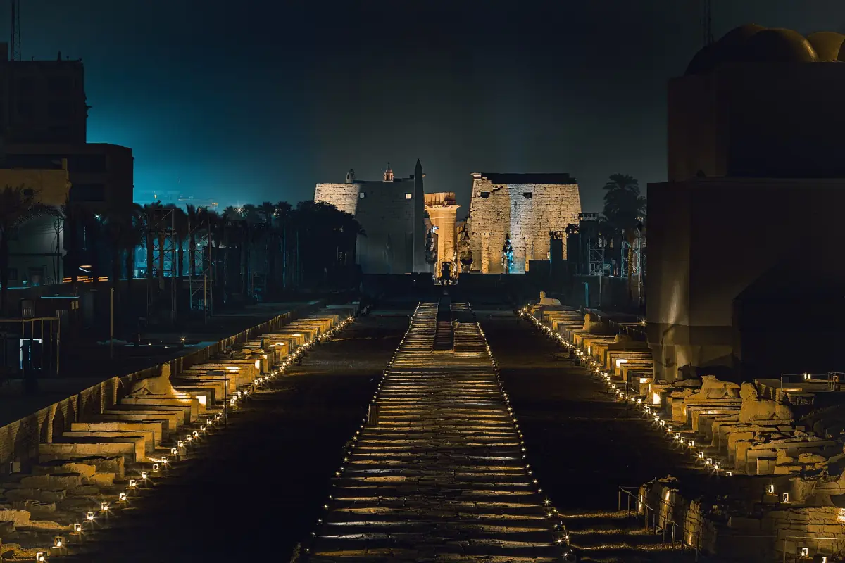 Avenue of sphinxes lit by ground lights leading toward the temple at night