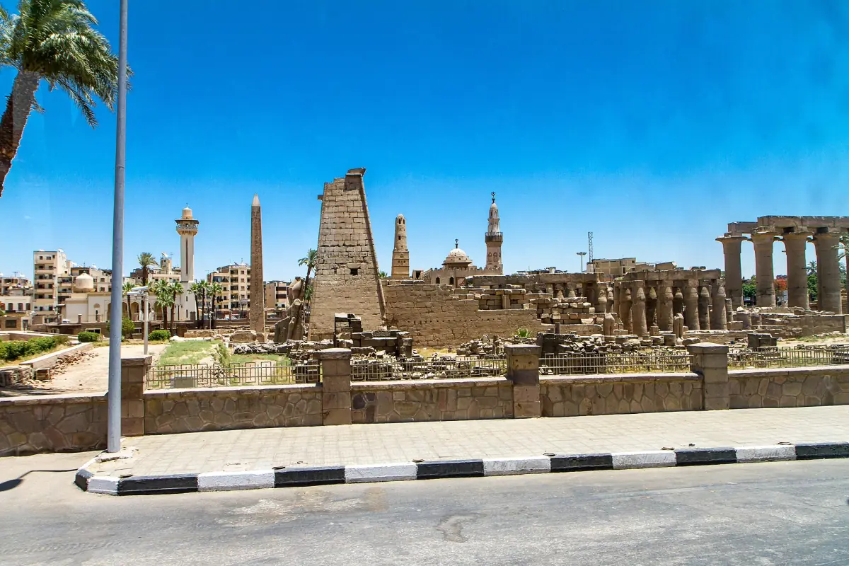 Luxor street with the temple pylon and ruins visible behind palm trees