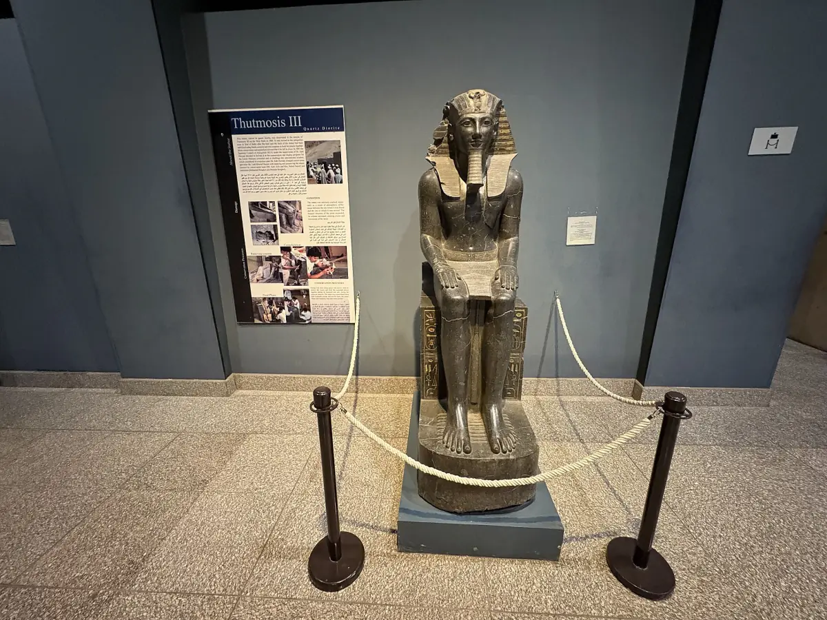 Statue royale debout dans une salle de musée avec un panneau d’information